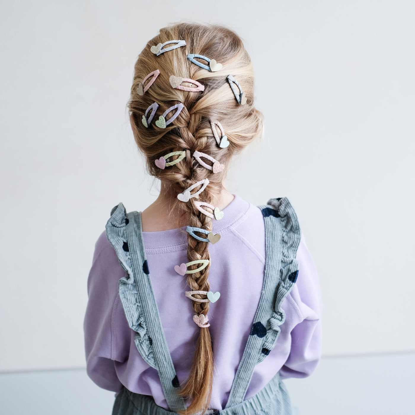 girl with her hair styled in a french plait with lots of heart mini clic clacs in it