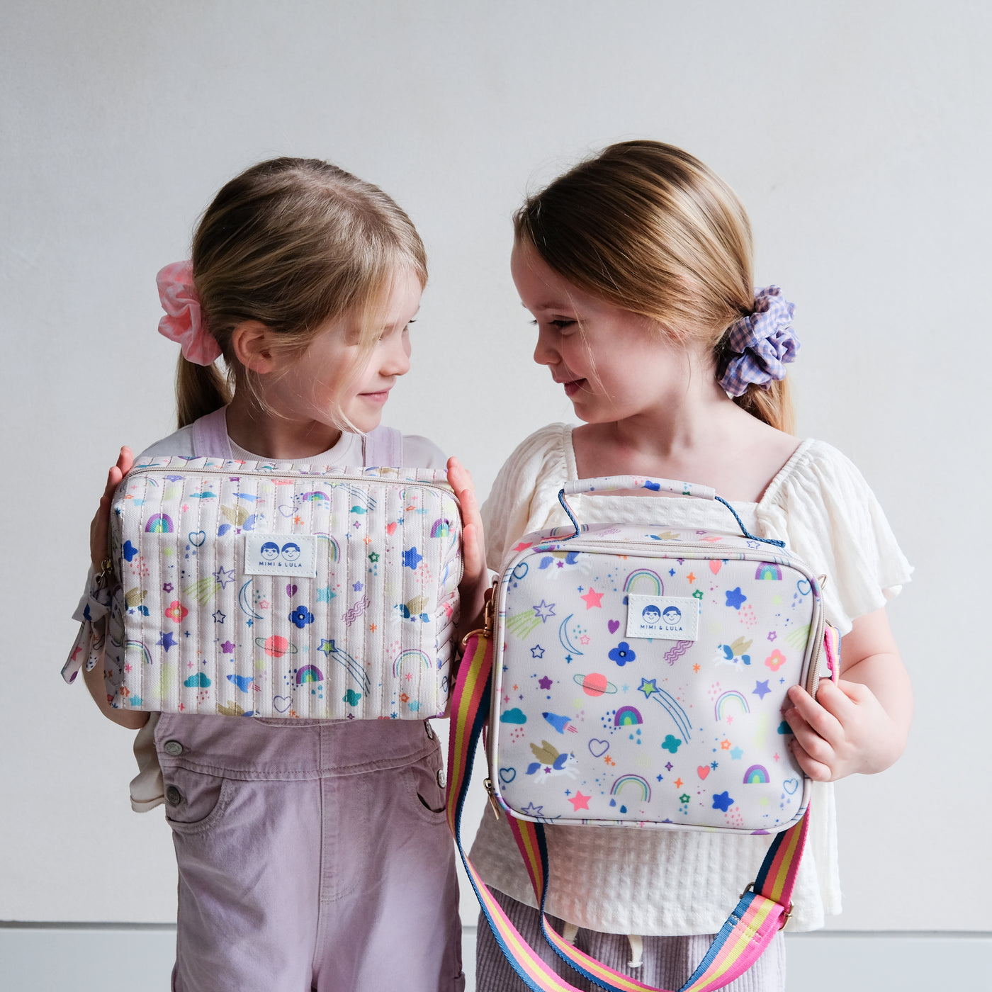 Two friends holding a lunch bag and a ash bag in a fun unicorn print, brightly coloured fabric