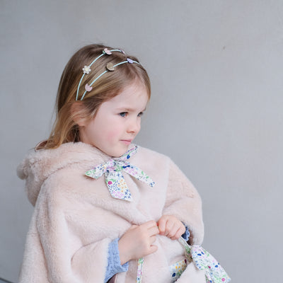 Little girl wearing a fluffy bunny cape for dressing up with hood including embroidered face, fluffy ears and a floral print fabric bow with popper to neck and satin lining and an Easter themed double alice band