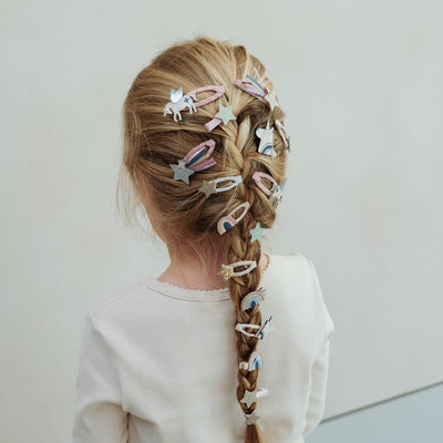 Child with braided hair adorned with colorful hair clips on a plain background