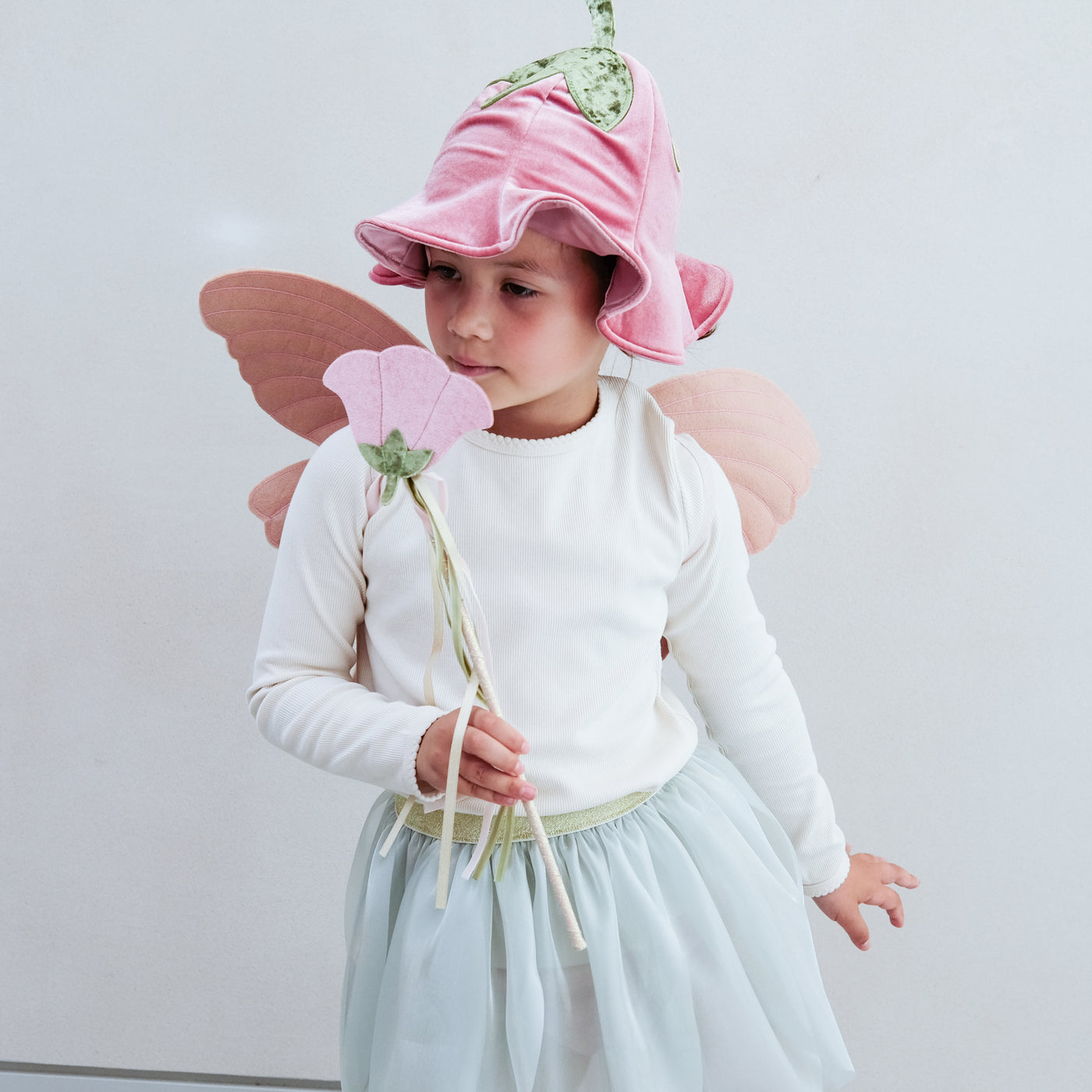 Child wearing a full flower fairy dress up set including velvet wings, velvet hat with stalk, soft green tutu and flower wand with ribbon trails
