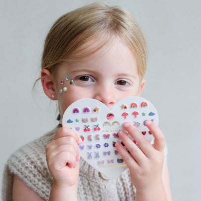 Child holding two heart-shaped sticker sheets with various designs on a plain background