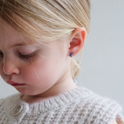 Close-up of a young girl wearing a small blue earring with a plain background
