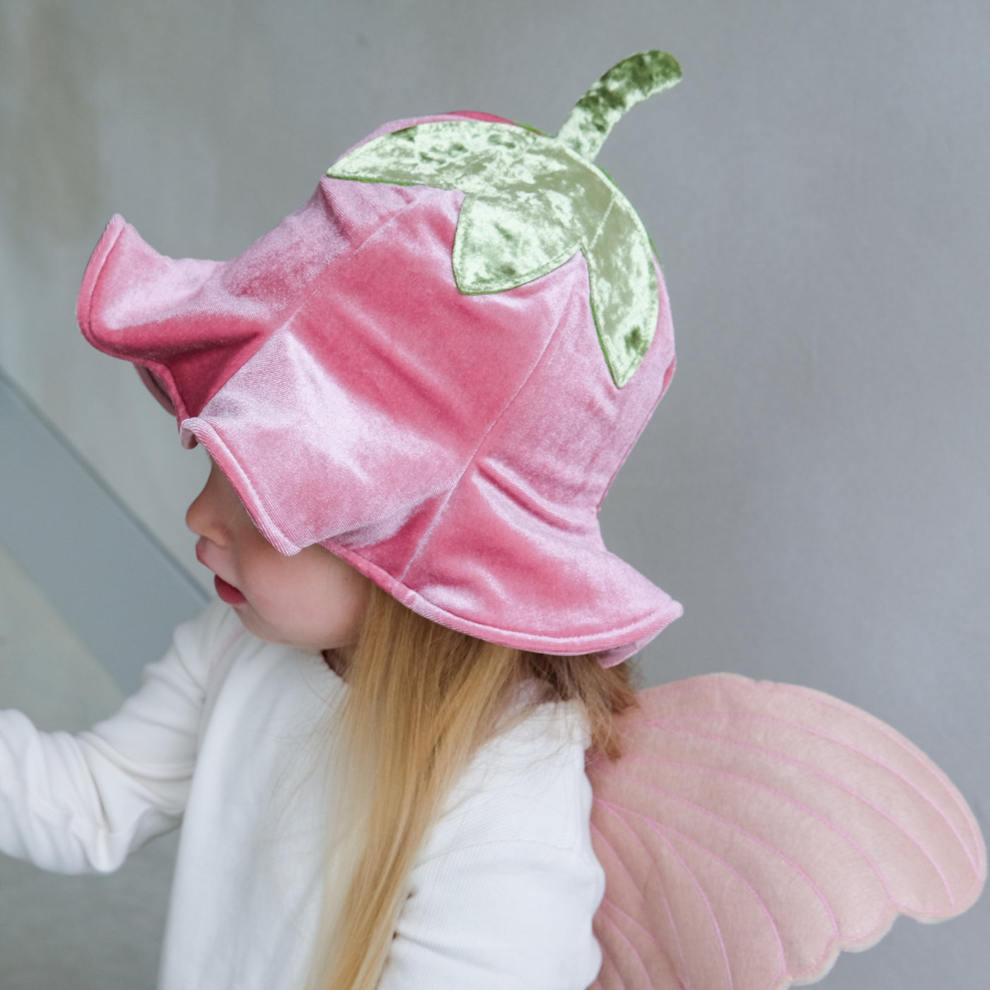 Child wearing a full flower fairy dress up set including velvet wings, velvet hat with stalk, soft green tutu and flower wand with ribbon trails
