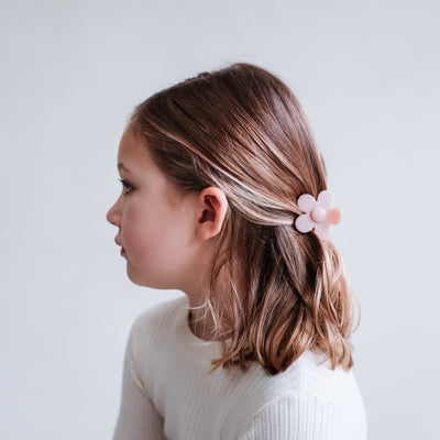 Soft pink daisy bulldog clip securing a part up hair do on a young, dark blonde little girl