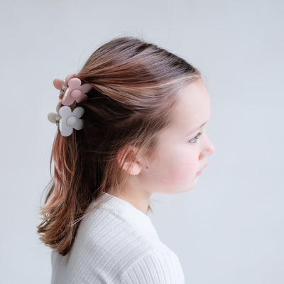 Little girl in a white ribbed top with hair partly up and secured by two pretty daisy shaped bulldog clips