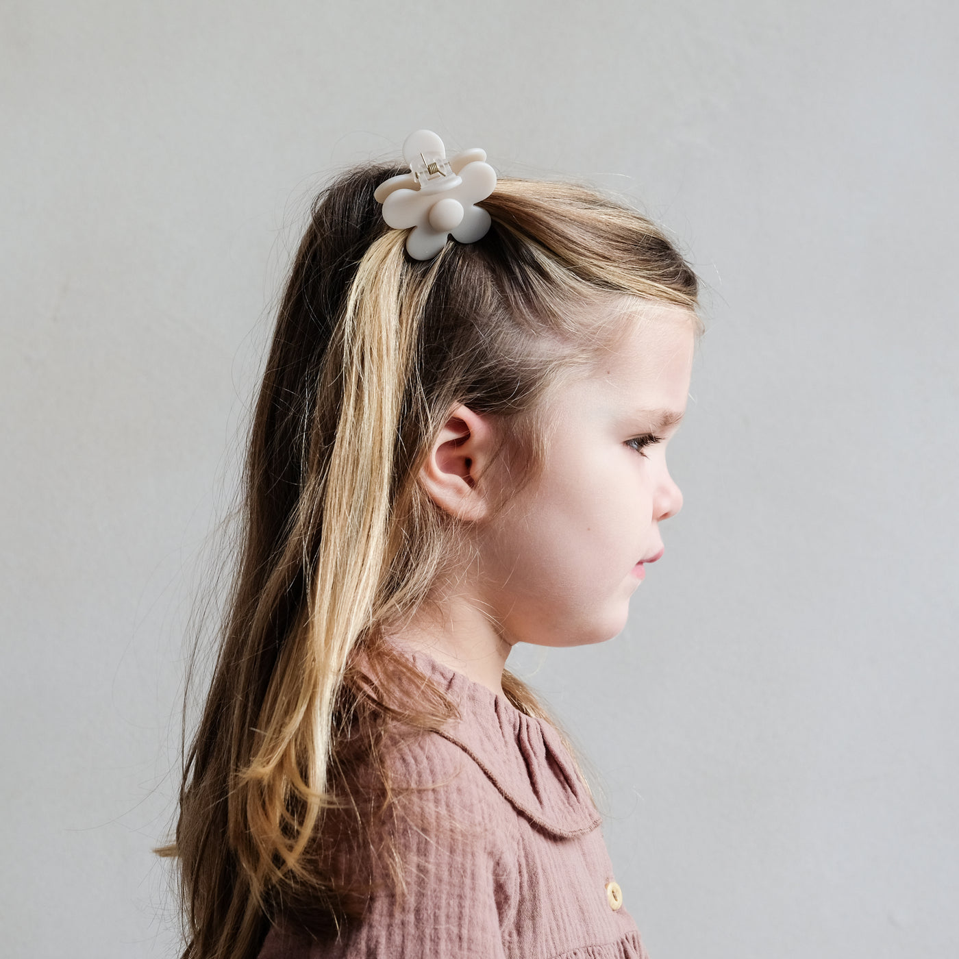 Little girl with hair partly clipped back using a pretty cream coloured daisy shape bulldog clip