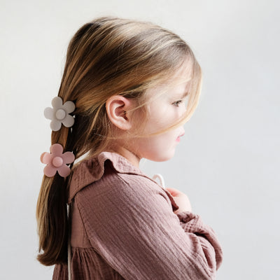 Side profile of dark blonde little girl with hair clipped back using two daisy shaped, neutral toned bulldog clips