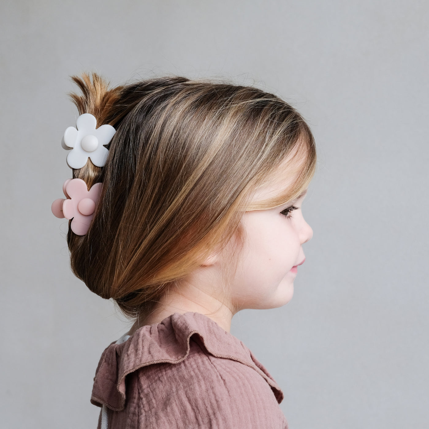 Side profile of little girl with pretty up do hair held together with two daisy shaped bulldog clips