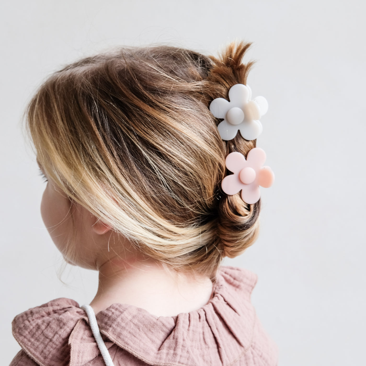 Dark blonde little girl with a twisted up do secured by beautiful daisy shaped bulldog clips in pale pink and cream