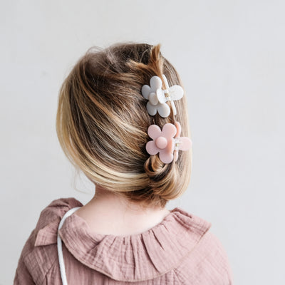 Little girl in dusky pink collared dress wearing two daisy shaped bulldog clips in a relaxed hair up style