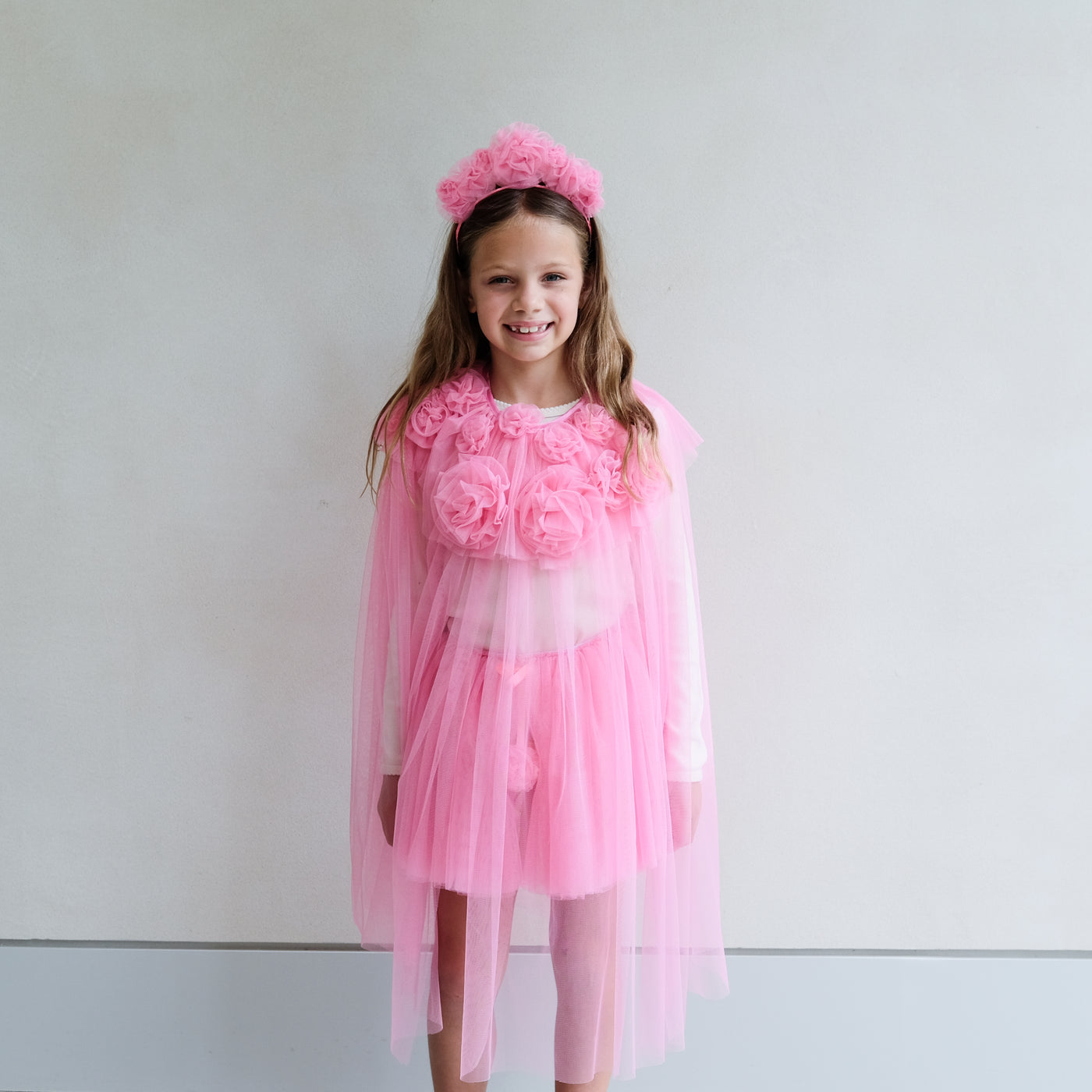 Video of young girl wearing a bright pink cape, tutu, wand, and floral ruffle headdress