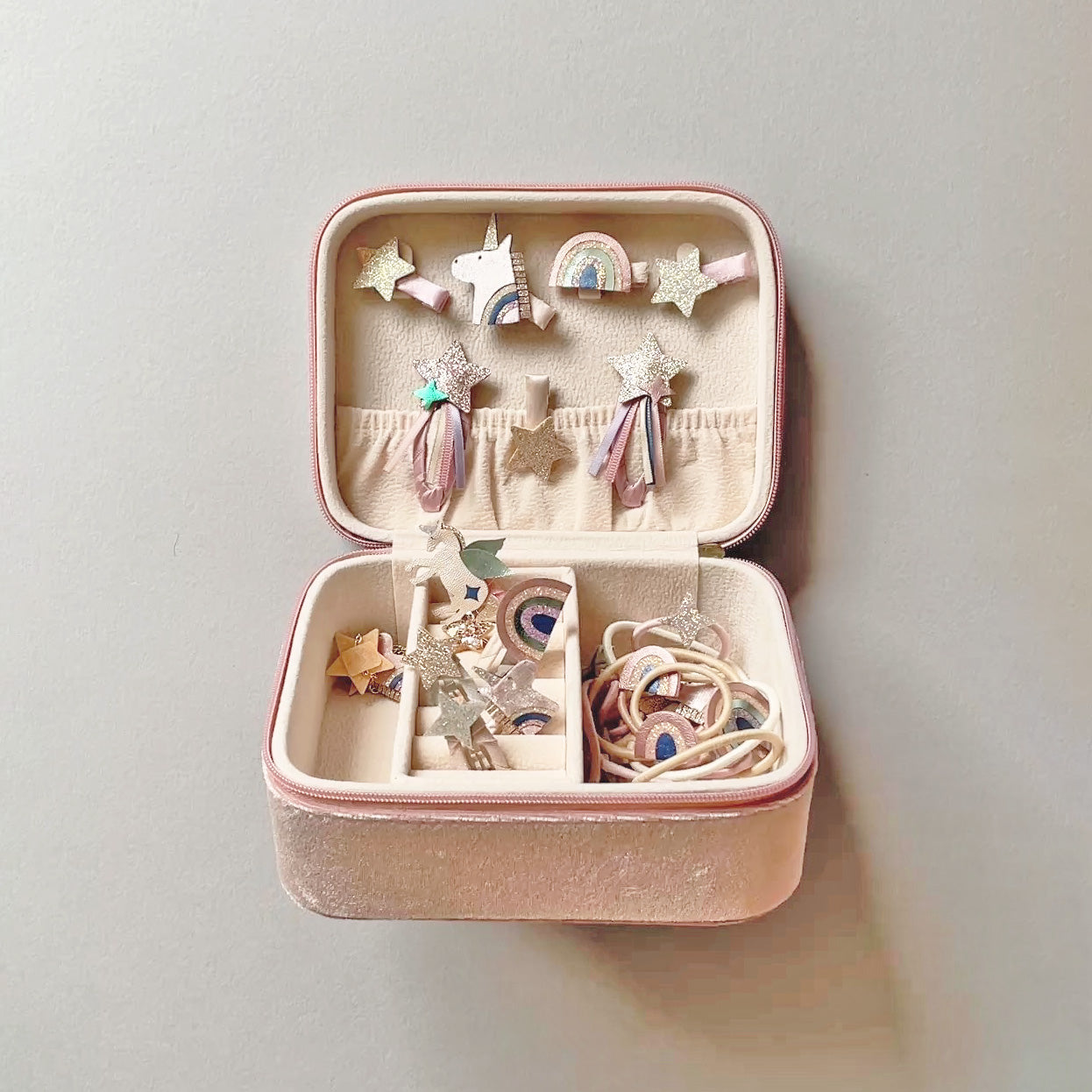 Pink unicorn jewellery box filled with unicorn hair accessories against a grey background